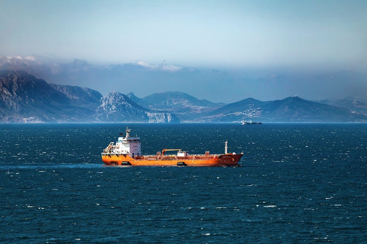 A small tanker crossing blue water with mountains behind