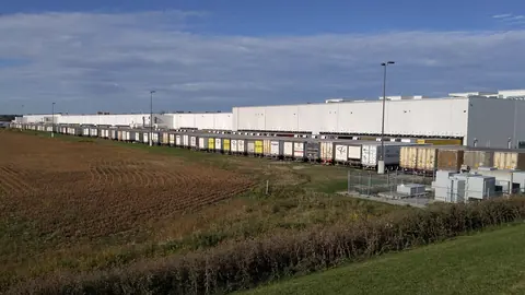 A long white warehouse with a line of trailers along its docks