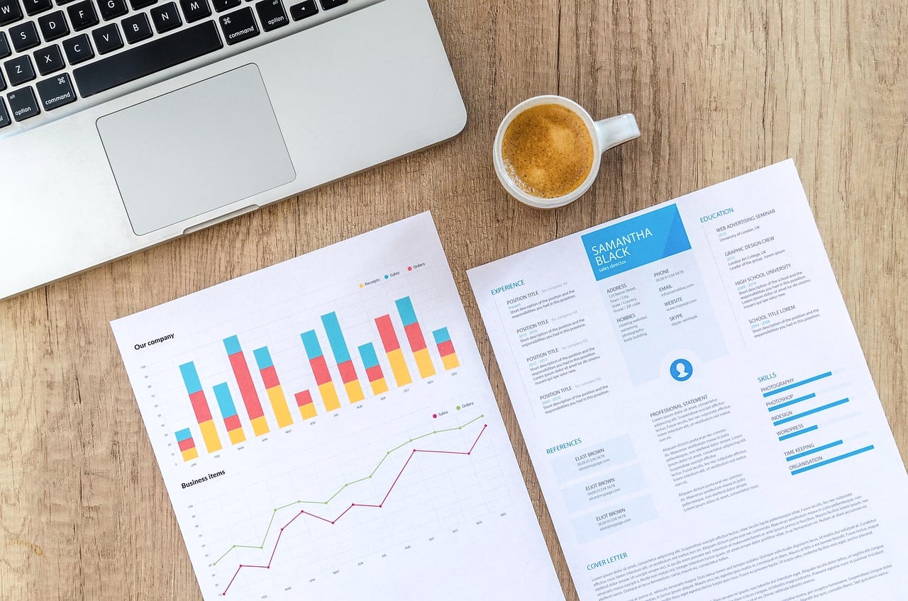 Printed charts and a report on a desk beside a laptop