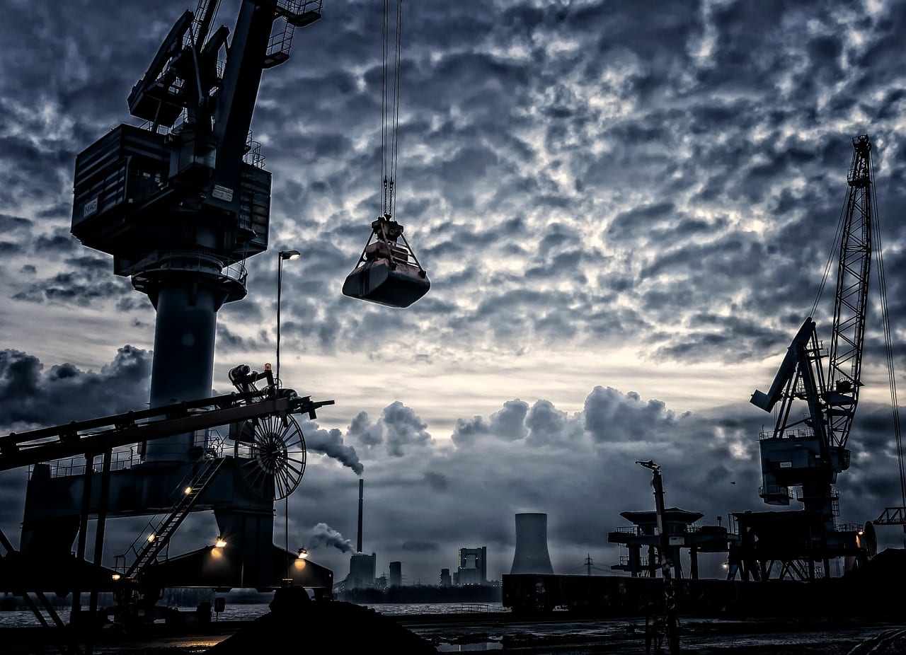 Dock cranes in silhouette against a sky of broken cloud