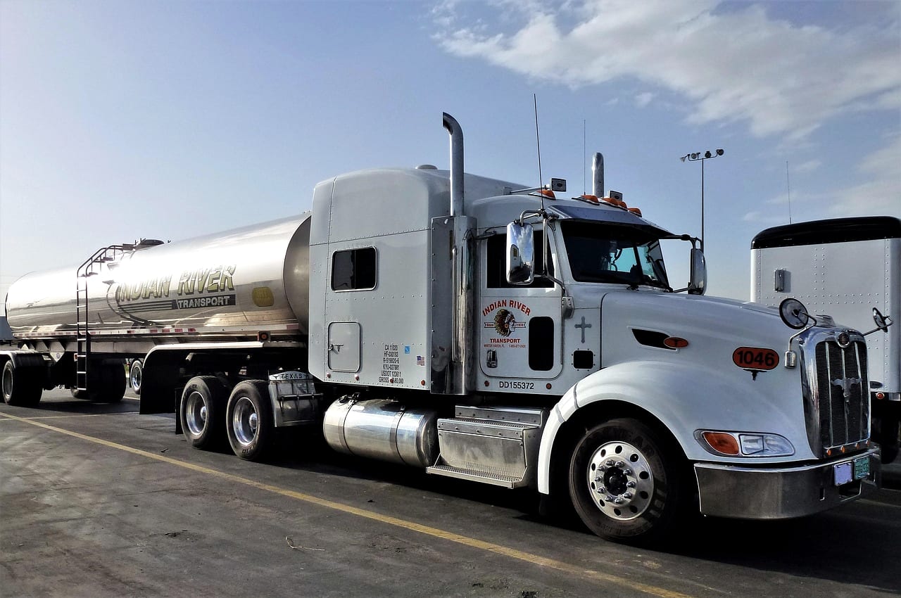 A white tractor hauling a polished steel tank trailer