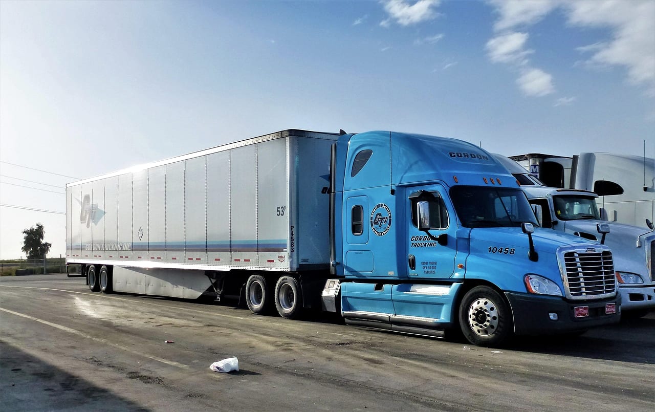 A blue tractor with a white trailer parked in a truck lot