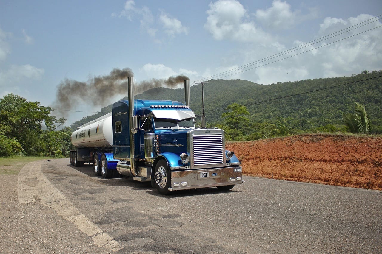 A truck trailing dark exhaust as it climbs a rural road