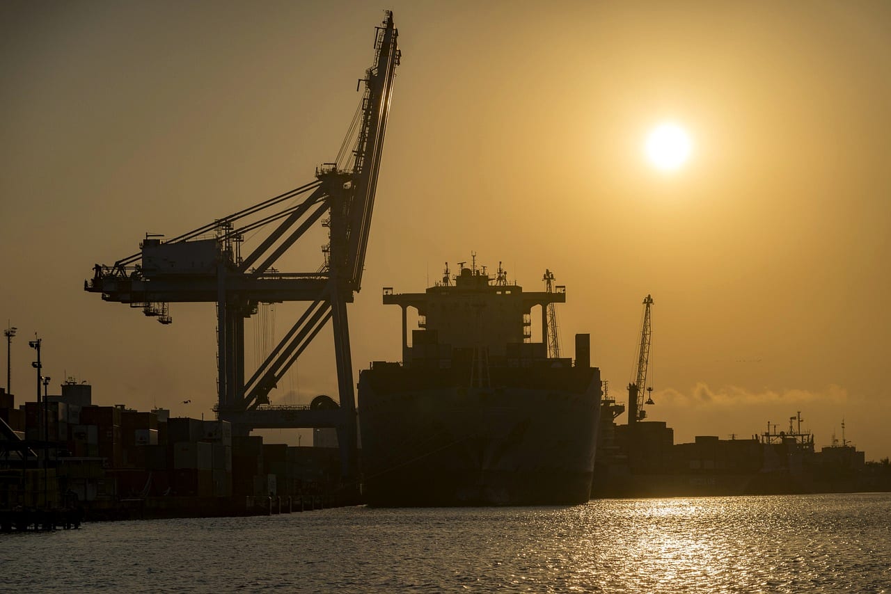 A harbor crane in silhouette against a hazy sun