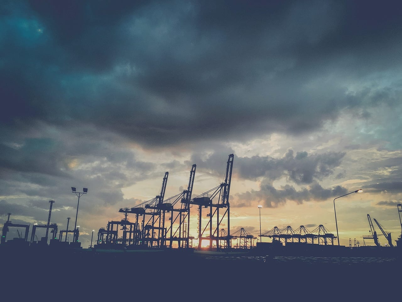 Port cranes in silhouette under a darkening, clouded sky