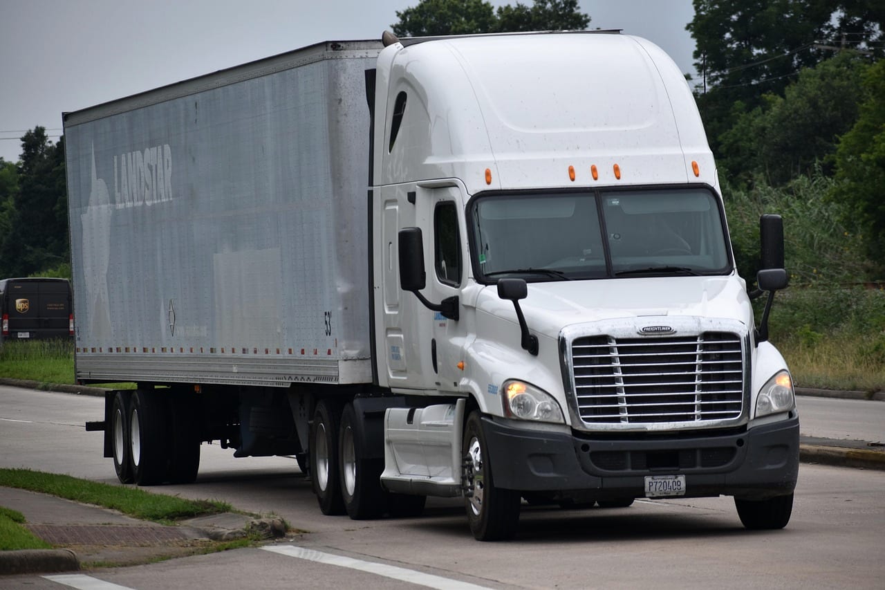 A white tractor pulling an unmarked dry van trailer on a two-lane road