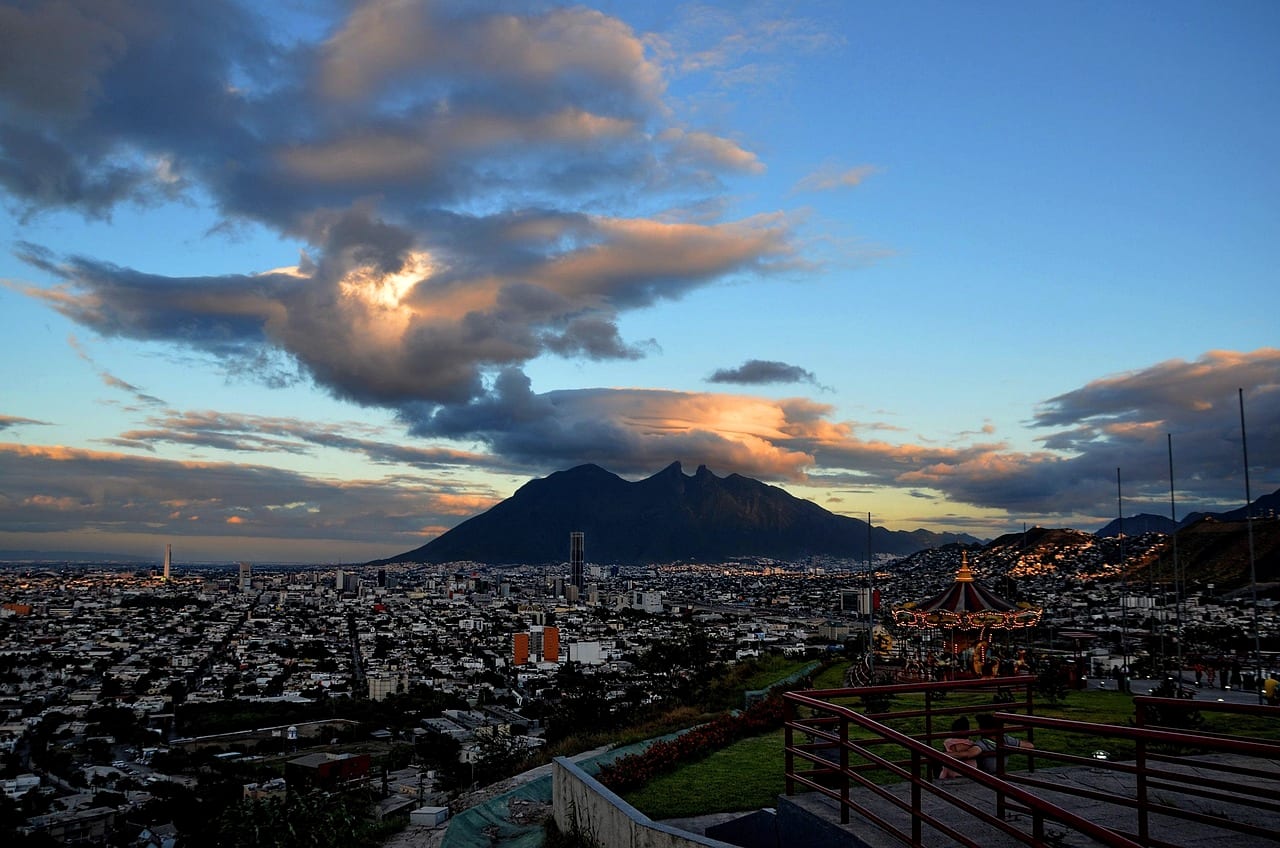 A city spread across a valley beneath a saddle-shaped mountain at dusk