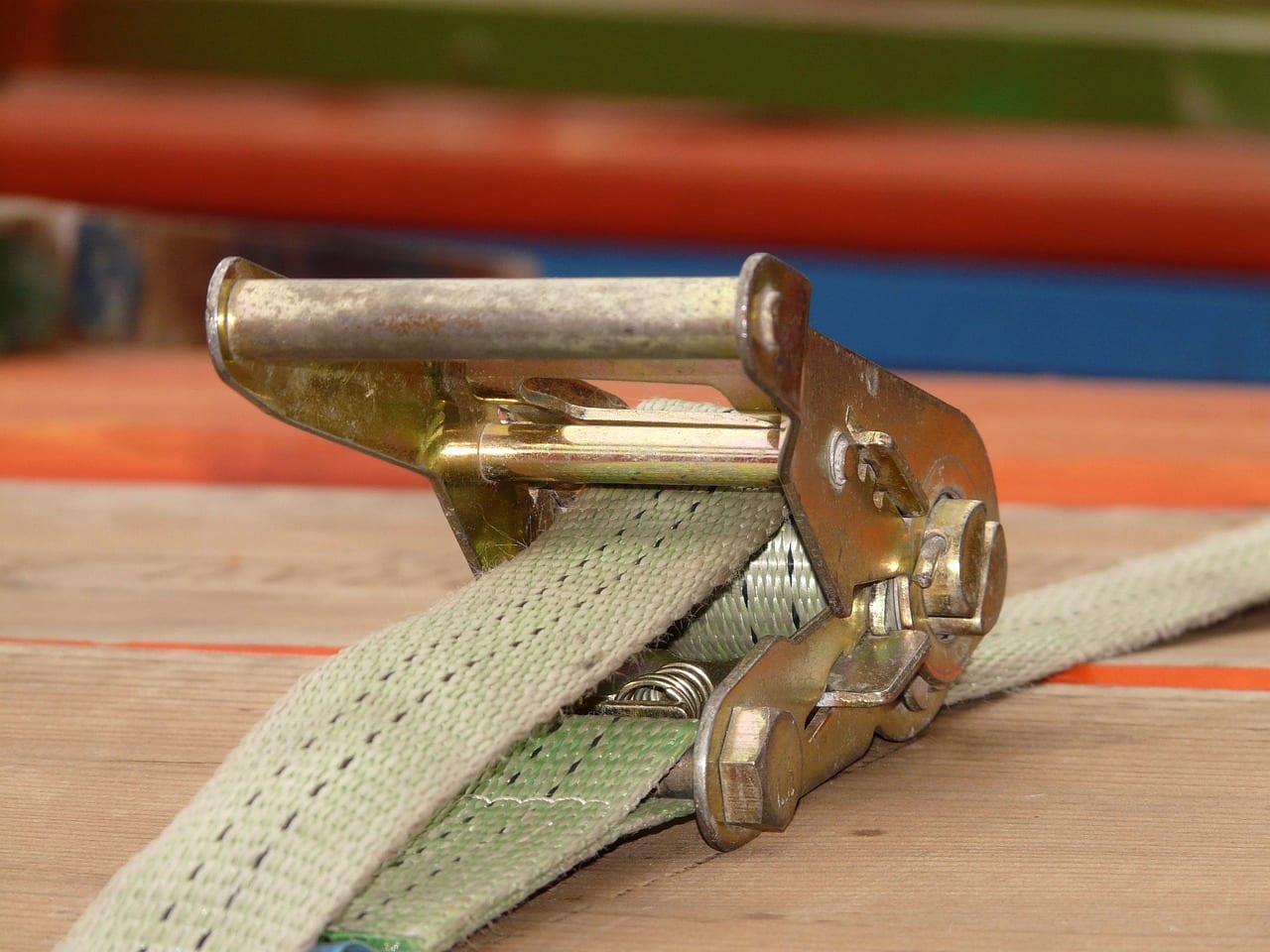 A ratchet strap tensioned over cargo on a wooden deck, close up