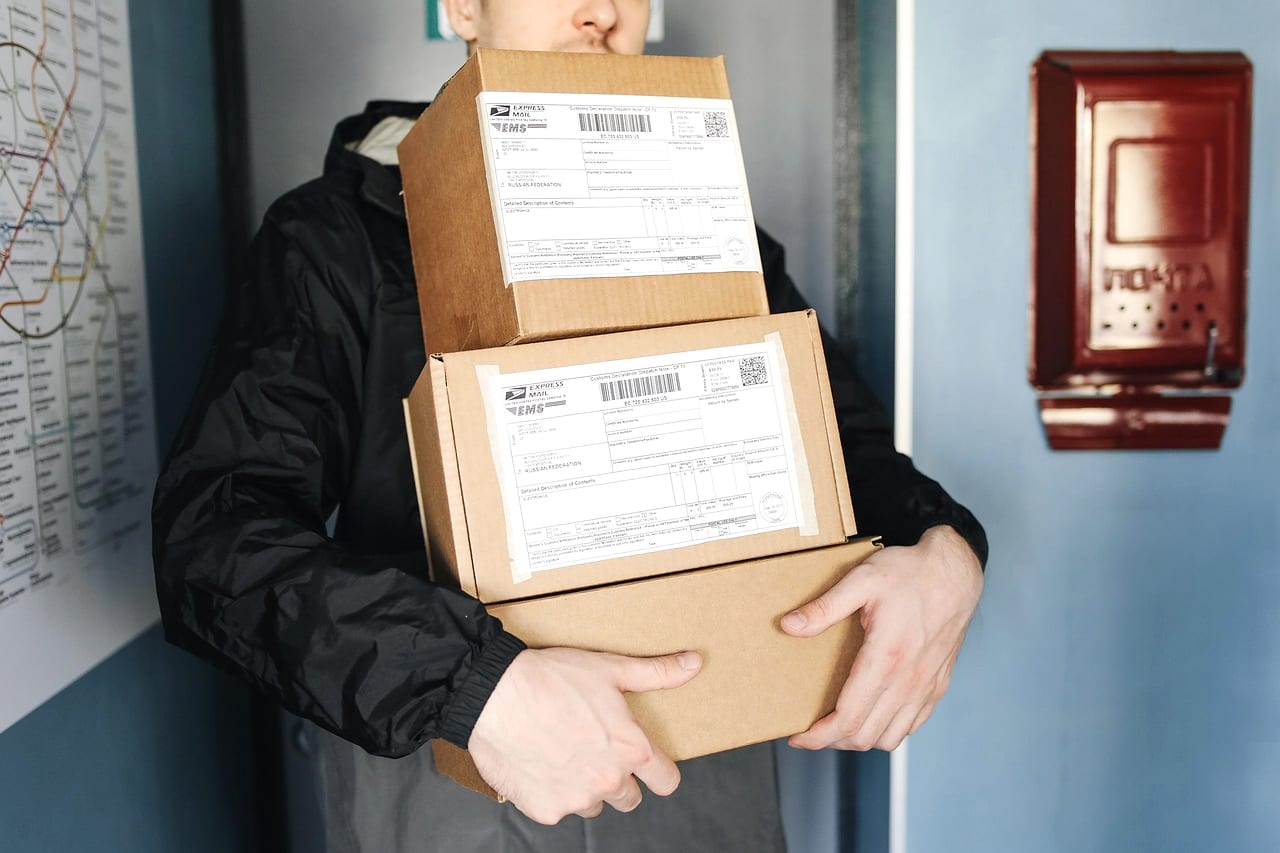 A courier carrying a stack of labeled parcels