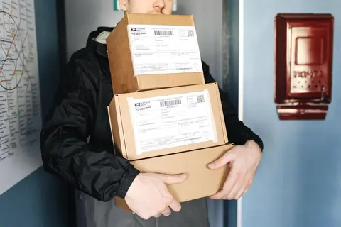 A courier carrying a stack of labeled parcels