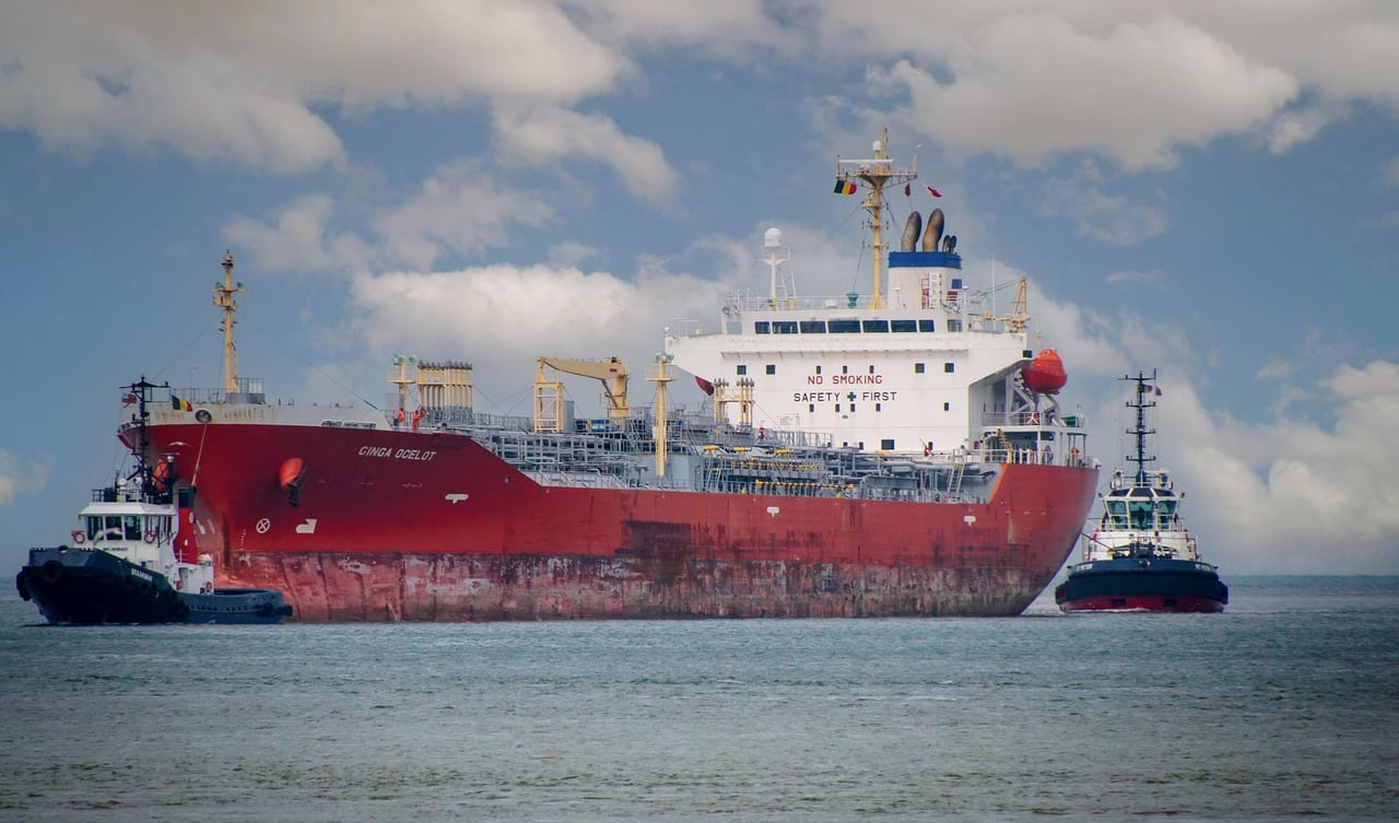 A red tanker being turned by two tugs