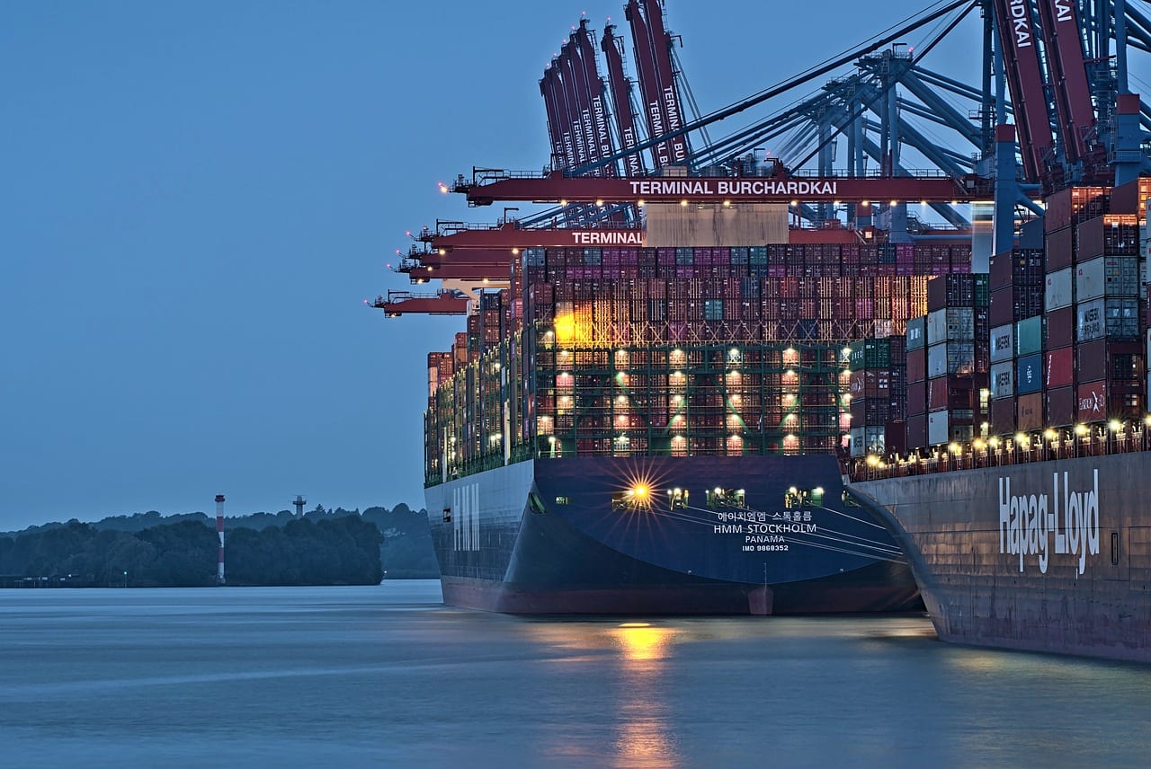 A container ship alongside a terminal at blue hour, cranes working above it