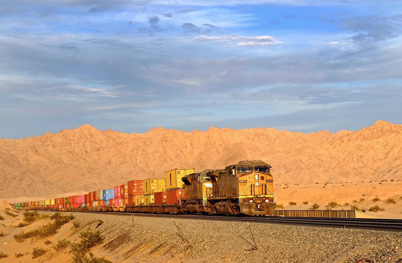 A double-stack container train crossing desert below sandstone hills
