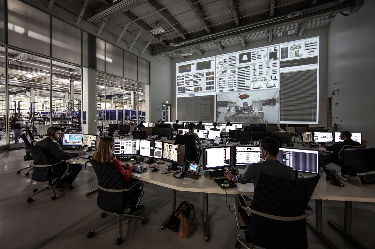 An operations center with staff at desks facing a wall of screens