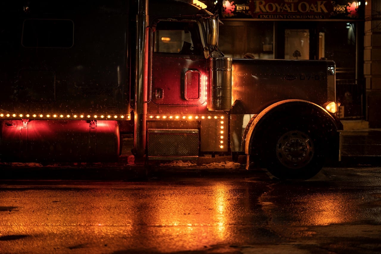 A tractor's marker lights reflected on wet asphalt at night