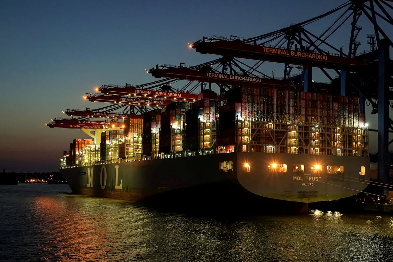 A container ship under floodlit cranes at night