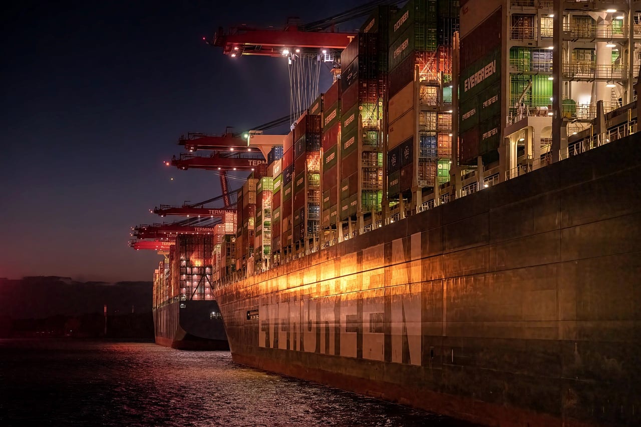 The hull of a container ship glowing under terminal lights at night