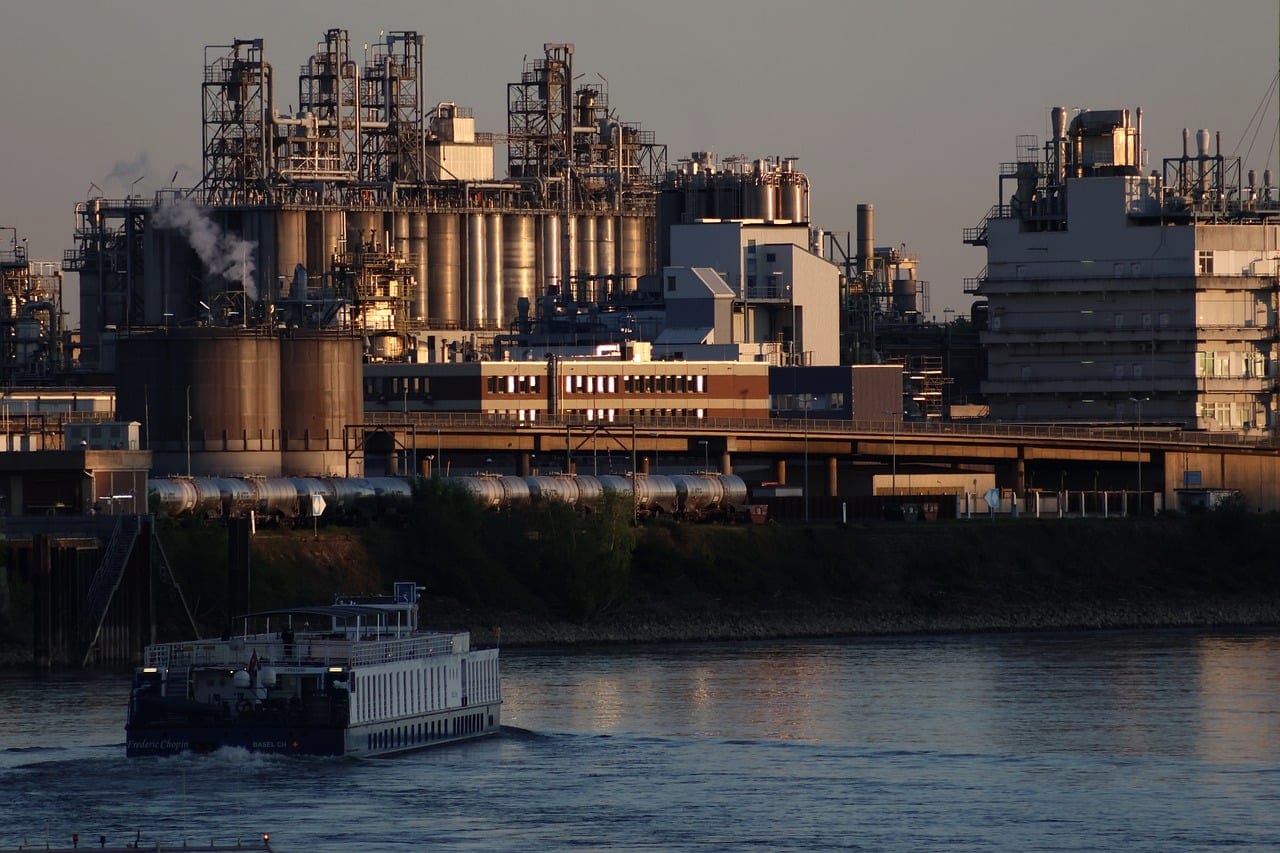 A chemical plant at dusk with a barge passing on the river in front