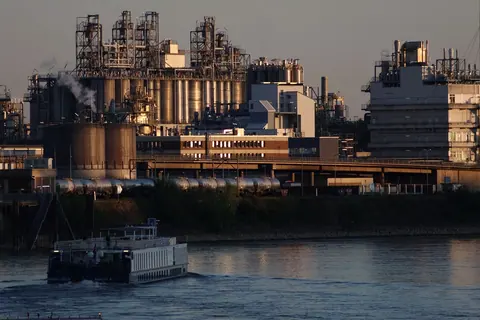 A chemical plant at dusk with a barge passing on the river in front